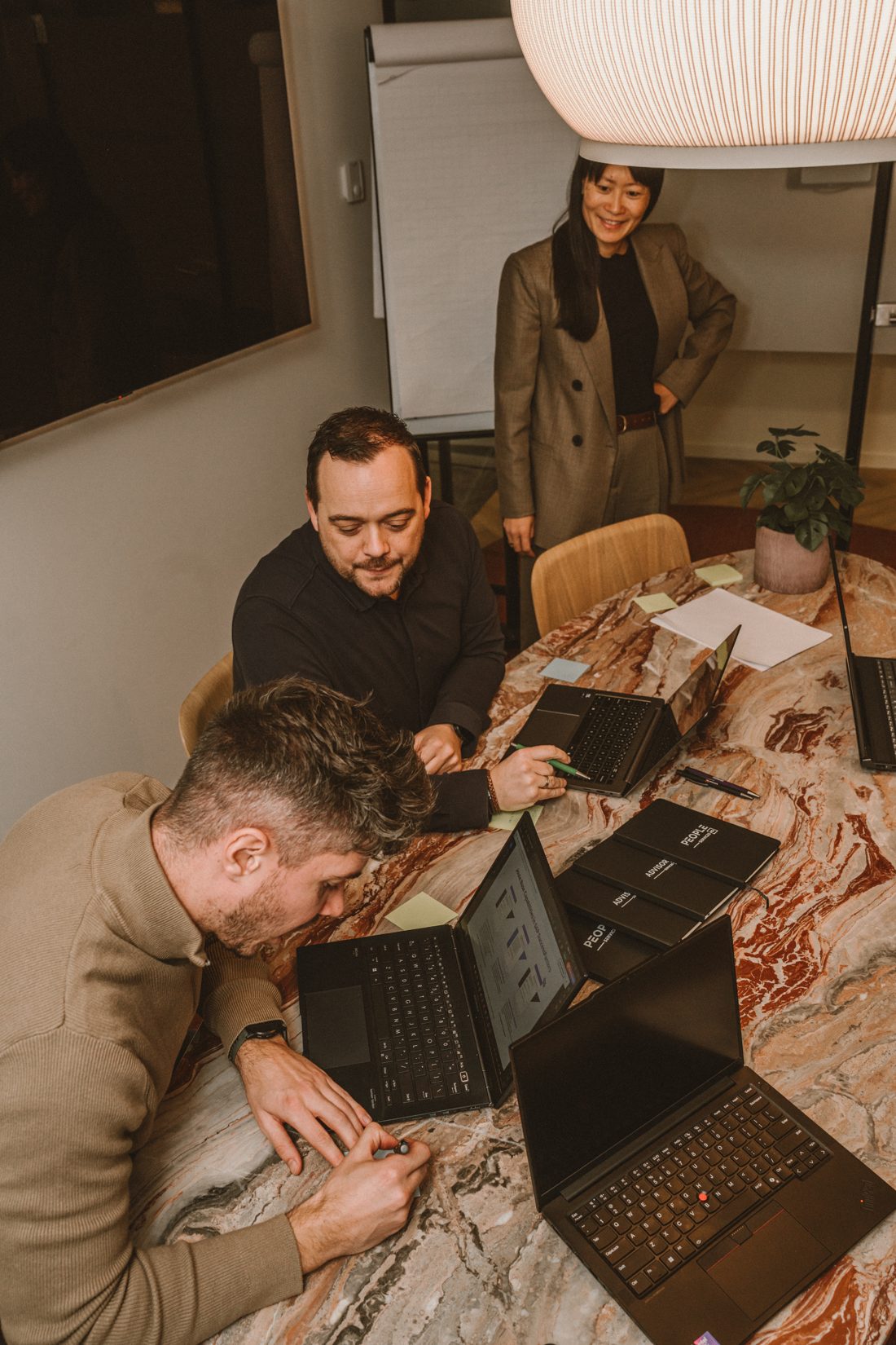 Drie mensen aan een tafel met laptops tijdens een werksessie